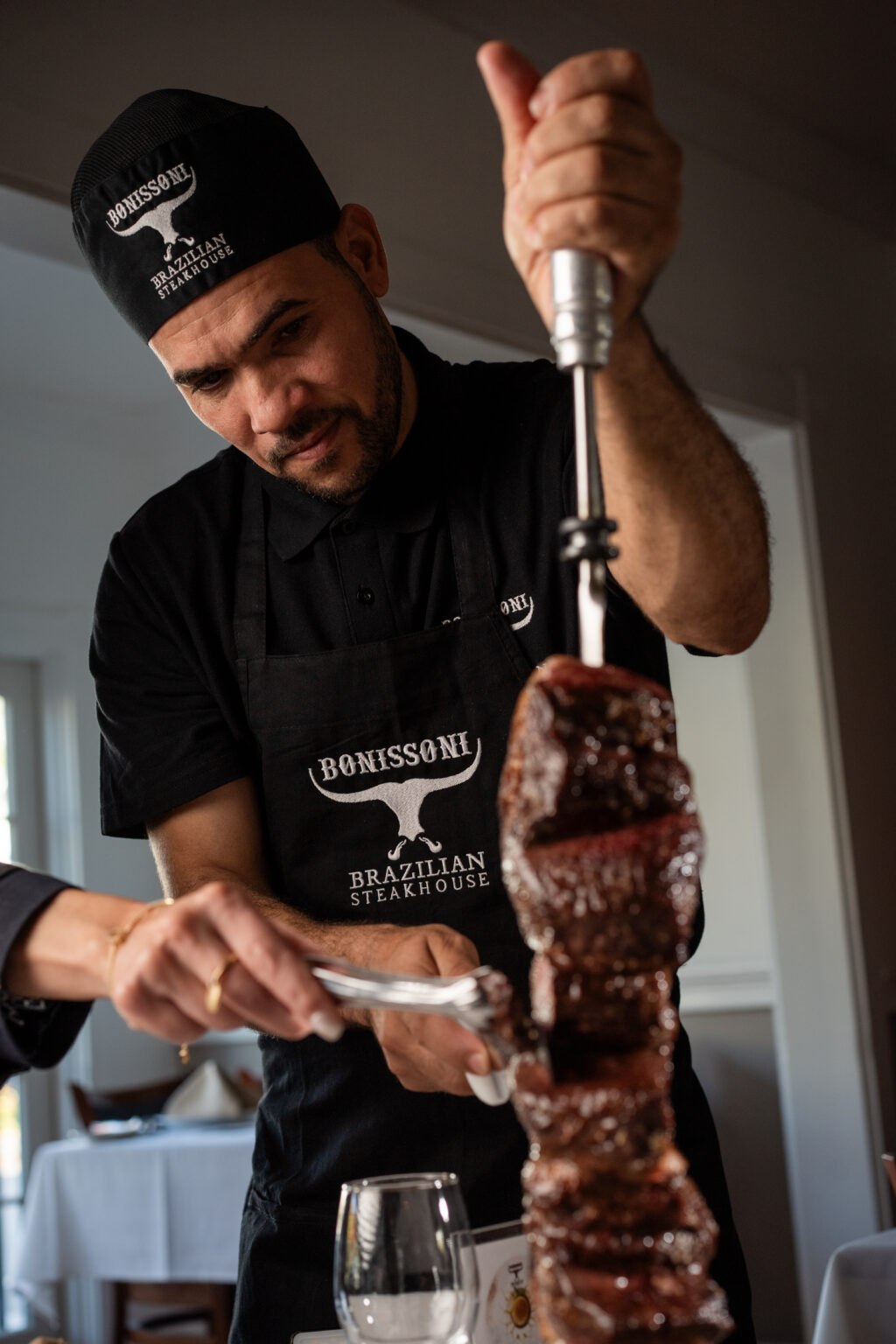 A Bonissoni gaúcho carving picanha from a skewer at a guest's table